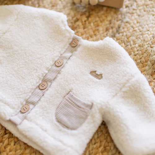 White baby sherpa jacket with buttons on a textured surface