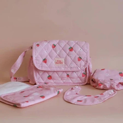 Pink quilted bag with strawberry pattern and matching pouches on a beige background